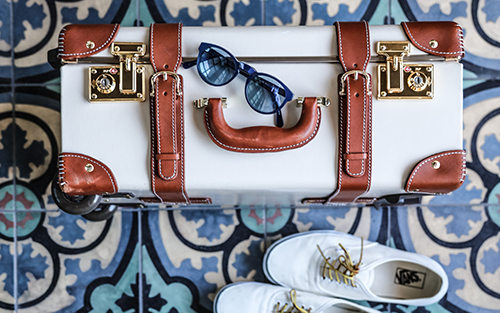Sunglasses on a suitcase, next to a pair of sneakers