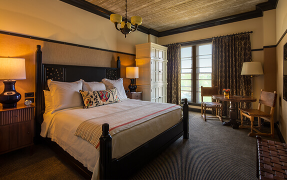 A picture of the bedroom in Hotel Emma's artesian rooms. Pictured is a king sized bed with nightstands and a table with two chairs.
