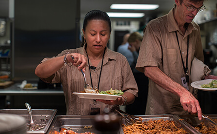 Woman and man serving food from cafeteria trays