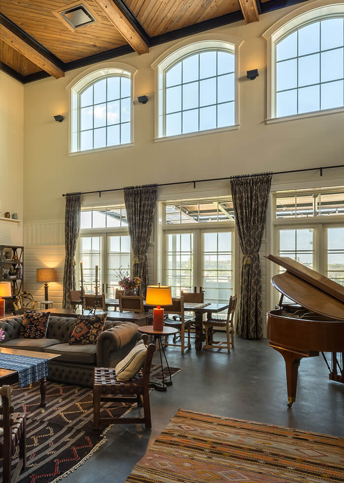 A picture of Hotel Emma's Emma Koehler suite option. Pictured is a brown piano, a grey couch, tall windows and a living room area with an 8 person table.